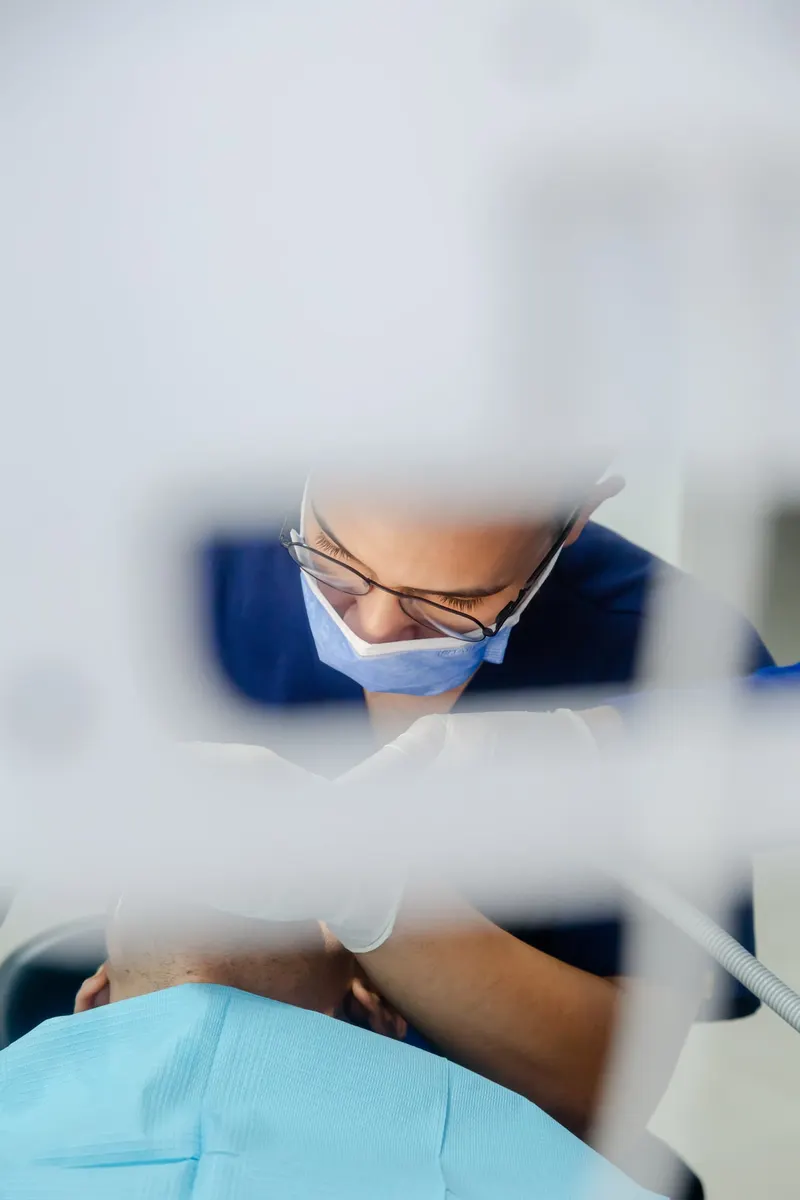 Dentist in blue scrubs treating a patient in the clinic - Dragonzay Photography