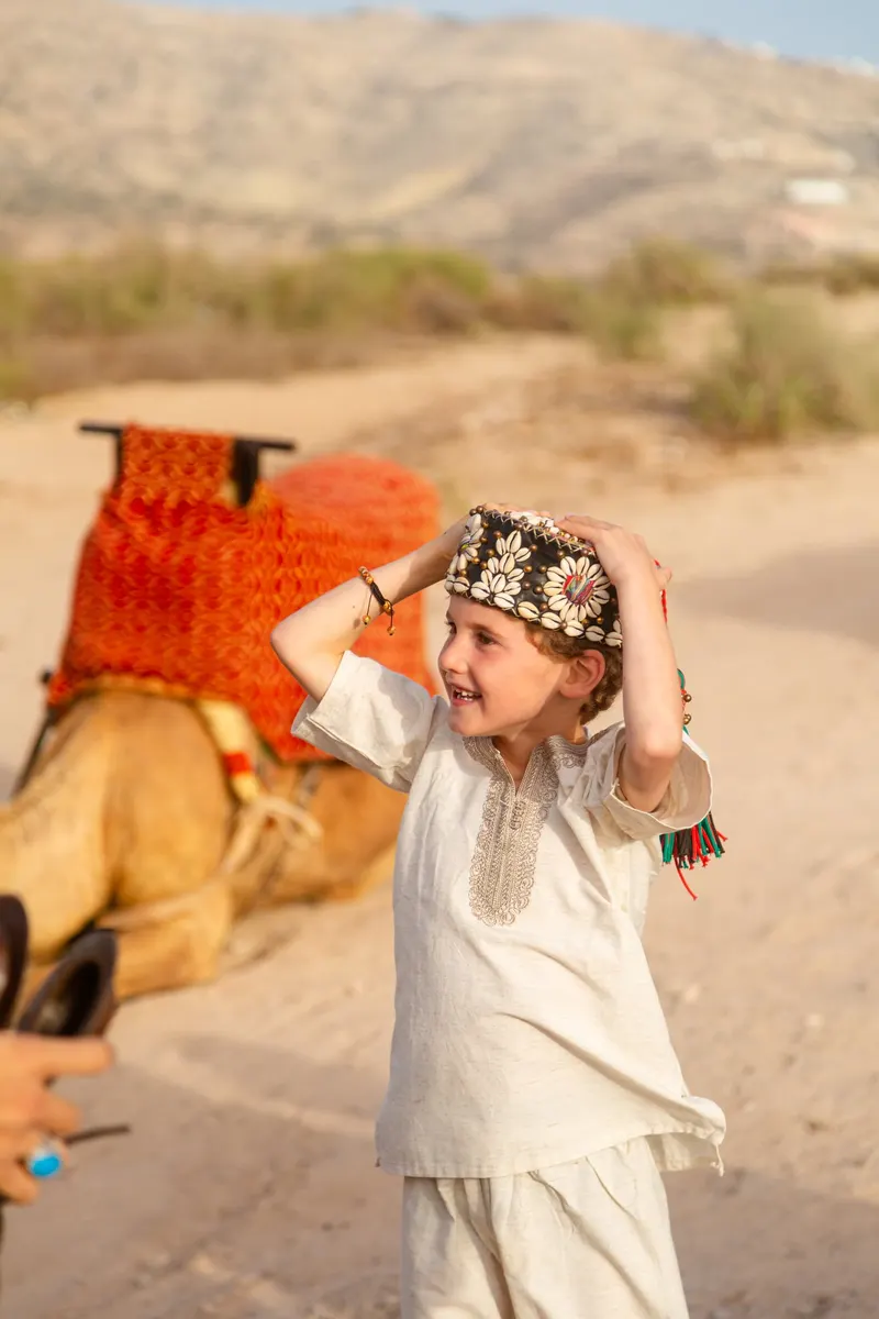Little girl in traditional dress beside a camel at a desert wedding - Dragonzay Photography