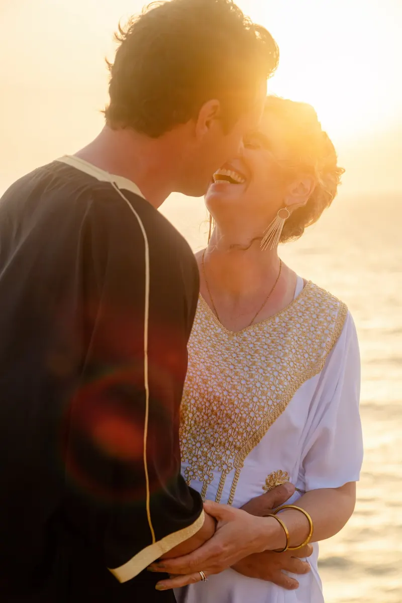 Newlyweds kissing against the sunset light on the beach - Dragonzay Photography