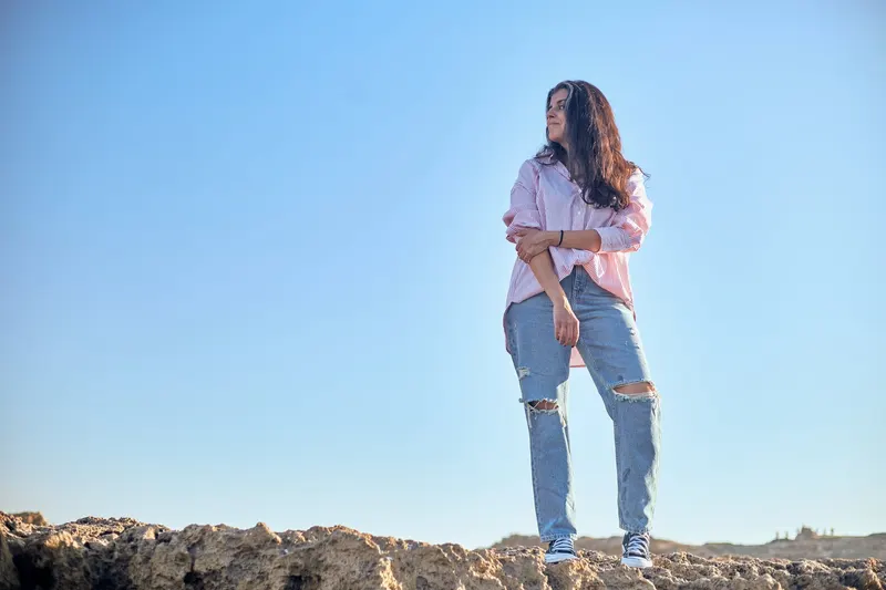 Young woman in jeans and a pink shirt on the rocky beach - Dragonzay Photography