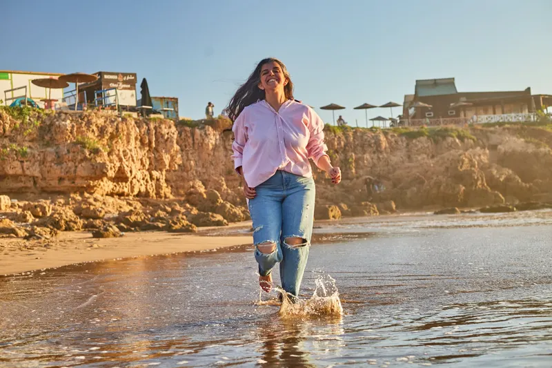 Young woman in jeans and a pink shirt on the rocky beach - Dragonzay Photography