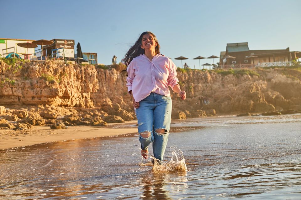 Jeune femme en jean et chemise rose sur la plage rocheuse - Dragonzay Photography