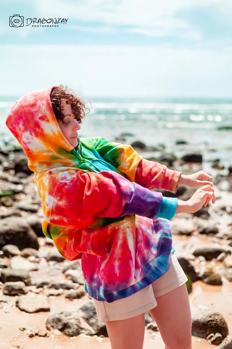 Joyful portrait in a multicoloured tie-dye hoodie on the beach - Dragonzay Photography