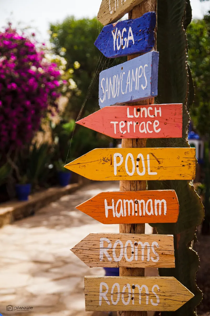 Wooden signpost pointing to pool, hammam, terrace and rooms - Dragonzay Photography